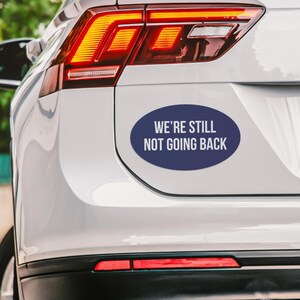 May include: A white car with a blue oval sticker that says "We're still not going back".