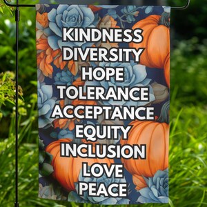 May include: A garden flag featuring the words "Kindness, Diversity, Hope, Tolerance, Acceptance, Equity, Inclusion, Love, Peace" in white text. The background has a floral design with blue, orange, and green elements, and orange pumpkins.