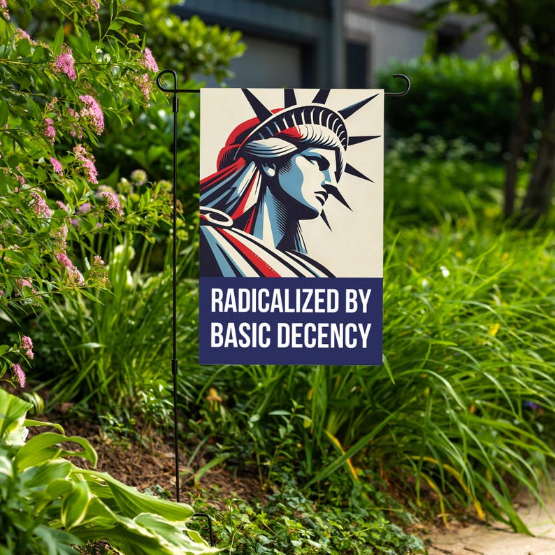 Może przedstawiać: Flaga ogrodowa z wystylizowaną ilustracją Statuy Wolności w kolorach czerwonym, białym i niebieskim. Flaga zawiera napis "RADICALIZED BY BASIC DECENCY" w kolorze białym na granatowym tle.