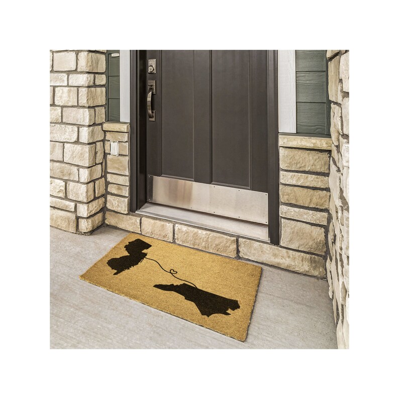 May include: A brown coir doormat with the outlines of New Jersey and North Carolina connected by a line with a heart in the middle. The doormat is in front of a brown door with a silver door kick plate.