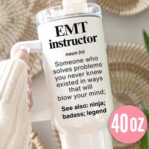 May include: A white 40 oz tumbler with a handle, featuring the text "EMT instructor" and a definition. The definition describes someone who solves problems. The tumbler also includes the words "ninja, badass, legend".