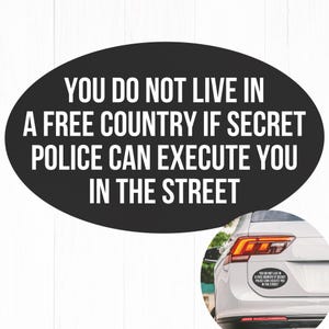 May include: Black oval bumper sticker with white text: "YOU DO NOT LIVE IN A FREE COUNTRY IF SECRET POLICE CAN EXECUTE YOU IN THE STREET." A car's rear is visible with the sticker applied.