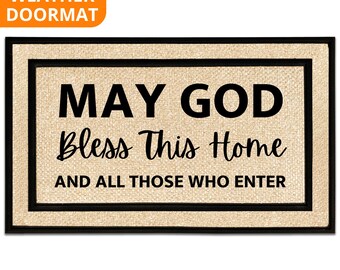 May include: Rectangular beige doormat with a black border. The text "MAY GOD Bless This Home AND ALL THOSE WHO ENTER" is printed in black. The top left corner has an orange banner that says "ALL WEATHER DOORMAT".
