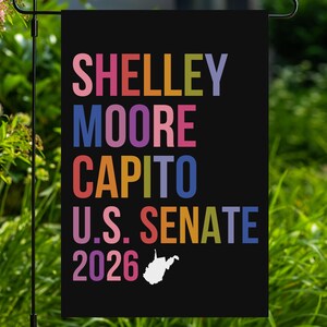 May include: A rectangular black garden flag featuring the multi-colored text SHELLEY MOORE CAPITO U.S. SENATE 2026. The letters are displayed in various shades of pink, blue, orange, yellow, and purple. A small white map of West Virginia is included.