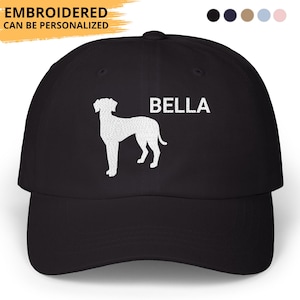 May include: Black baseball cap with the word "BELLA" in white, and a white dog silhouette. The cap has the text "EMBROIDERED CAN BE PERSONALIZED" in yellow. The cap has a curved brim and a fabric strap closure.