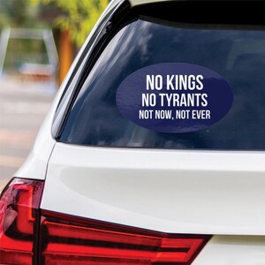 May include: An oval car sticker with the text "NO KINGS NO TYRANTS NOT NOW, NOT EVER" in white on a dark blue background. The sticker is affixed to the rear window of a white car.
