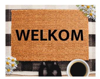 May include: A rectangular doormat with the word "WELKOM" in bold black letters. The mat is a light brown color and sits on a black and white checkered pattern. White daisies and a cup of coffee complete the scene.