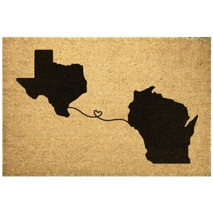 May include: A brown doormat with the outlines of Texas and Wisconsin in black, connected by a line with a heart in the middle.