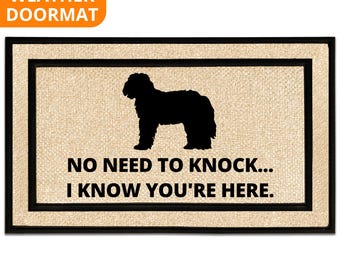 May include: Rectangular doormat with a black border and a tan center. A black silhouette of a dog is centered on the mat, with the text "NO NEED TO KNOCK... I KNOW YOU'RE HERE." The top left corner has the words "ALL WEATHER DOORMAT."