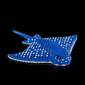 May include: A blue and white spotted stingray figurine. The toy ray has a detailed design with white spots and a curved tail. The figurine is set against a black background.