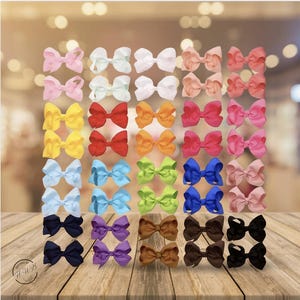 May include: A collection of colorful hair bows in various shades, including pink, white, yellow, red, orange, blue, green, brown, purple, and black. The bows are arranged in a grid pattern on a wooden surface, with a blurred background.