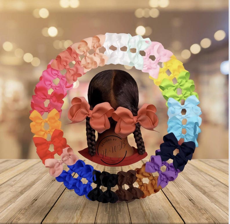 May include: A variety of colorful hair bows arranged in a circular pattern. The bows are in shades of pink, orange, yellow, green, blue, purple, black, brown, and white. The image also shows a person with two braids and large bows.