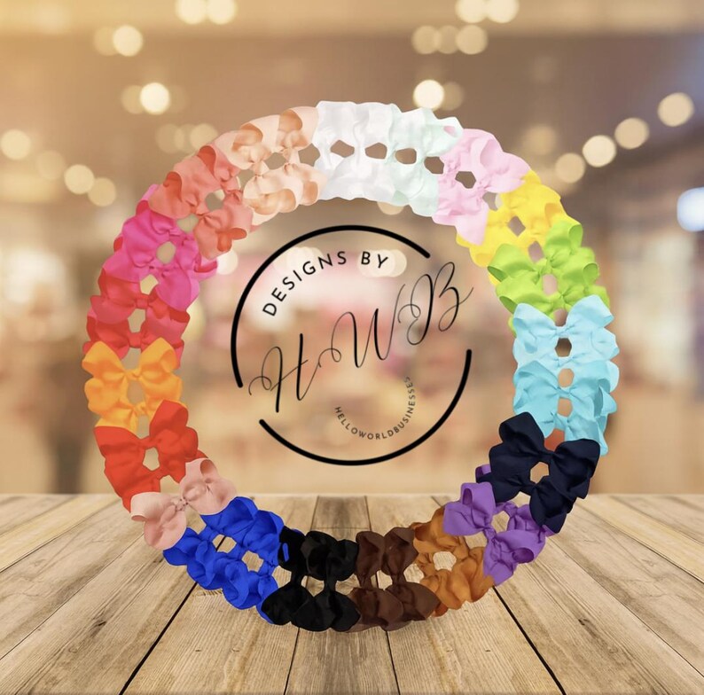May include: A circular arrangement of colorful hair bows in various shades, including pink, orange, blue, and purple. The bows are arranged around a central logo that reads "DESIGNS BY HWB" and "HELLOWORLDBUSINESS". The background is blurred.