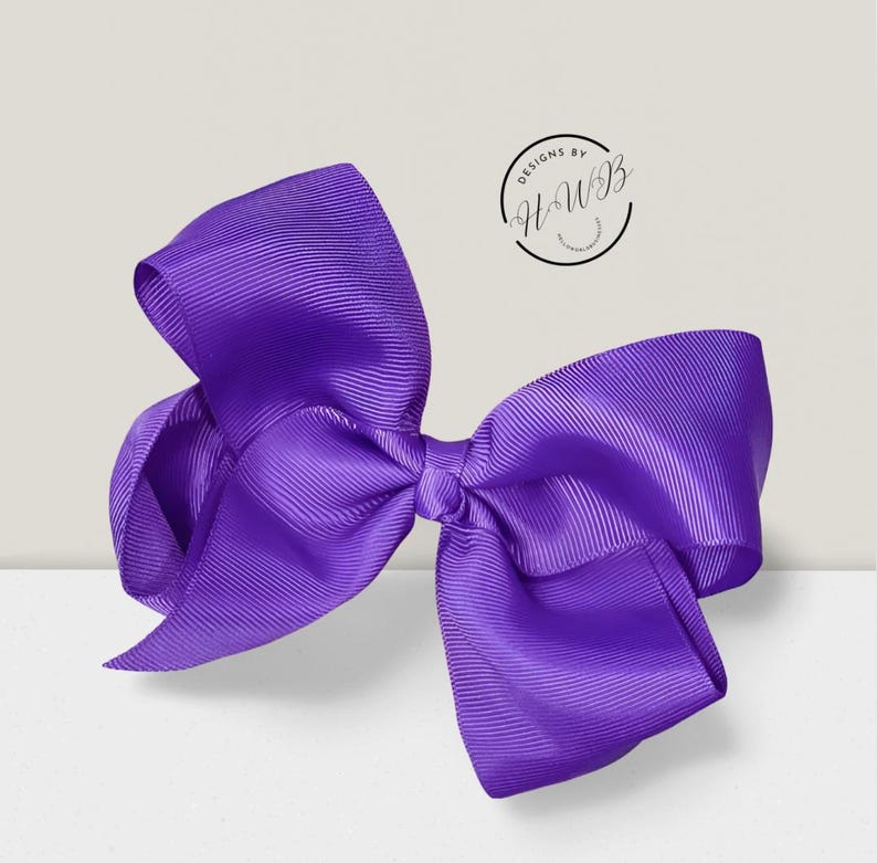 May include: A large, vibrant purple bow made of ribbed grosgrain ribbon. The bow is centered and has multiple loops and tails, creating a full, decorative appearance. The text "DESIGNS BY HWB" is in a circle in the upper right corner.