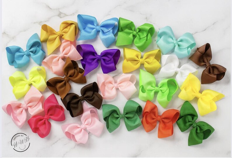 May include: A collection of colorful satin hair bows in various shades, including blue, yellow, pink, green, and brown. The bows are arranged on a white marble surface, showcasing their vibrant colors and textures. The bows are a popular accessory.