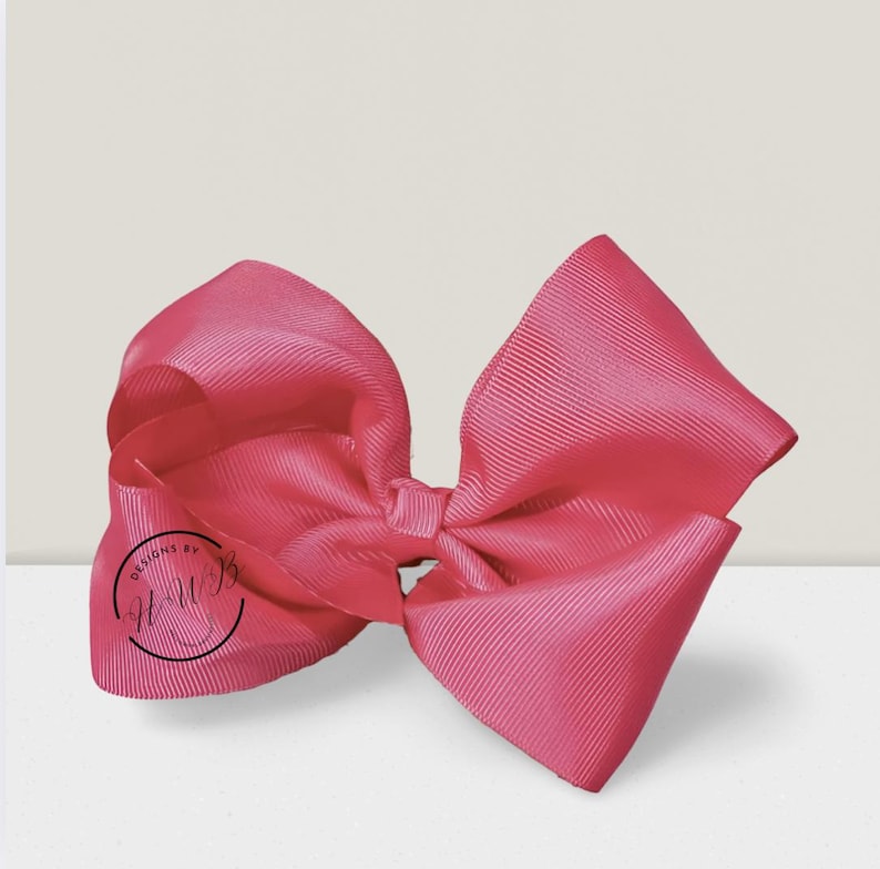 May include: A large, vibrant pink bow made of ribbed fabric. The bow is tied in the center and has a full, voluminous shape. The text "DESIGNS BY HWB" is printed on the left side of the bow in a black circle.