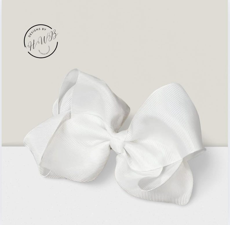 May include: A large, white hair bow made of ribbed grosgrain ribbon. The bow is centered and has a classic shape, with multiple loops and tails. The image includes the text "DESIGNS BY HWB" in a circular logo.