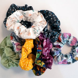 May include: A collection of colourful fabric scrunchies with various patterns, including floral, polka dot and geometric designs. The scrunchies are made of soft, stretchy fabric and are perfect for holding hair in place.