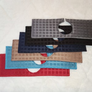 May include: A stack of six dishcloths in various colours, including red, blue, brown, black, and grey. Each cloth has a circular hole in the centre and a waffle-like texture.