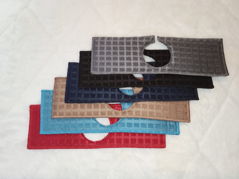 May include: A stack of six dishcloths in various colours, including red, blue, brown, black, and grey. Each cloth has a circular hole in the centre and a waffle-like texture.