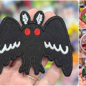 May include: A black felt iron-on patch of a bat with red eyes and white markings. The bat has a creepy, gothic aesthetic.