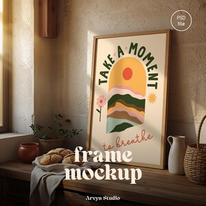 May include: A framed art print with the words "Take a Moment to Breathe" in a warm, neutral-toned room. The artwork features a landscape design with a sun, mountains, and a flower. The frame is a light wood color, and the overall aesthetic is minimalist and calming.