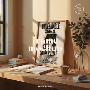 May include: A framed poster with the text "Undesirable No. 1 Harry Potter" is displayed on a wooden surface. The scene includes an open book, a coffee cup, and a vase with greenery, creating a cozy, inviting atmosphere. The frame is light brown.