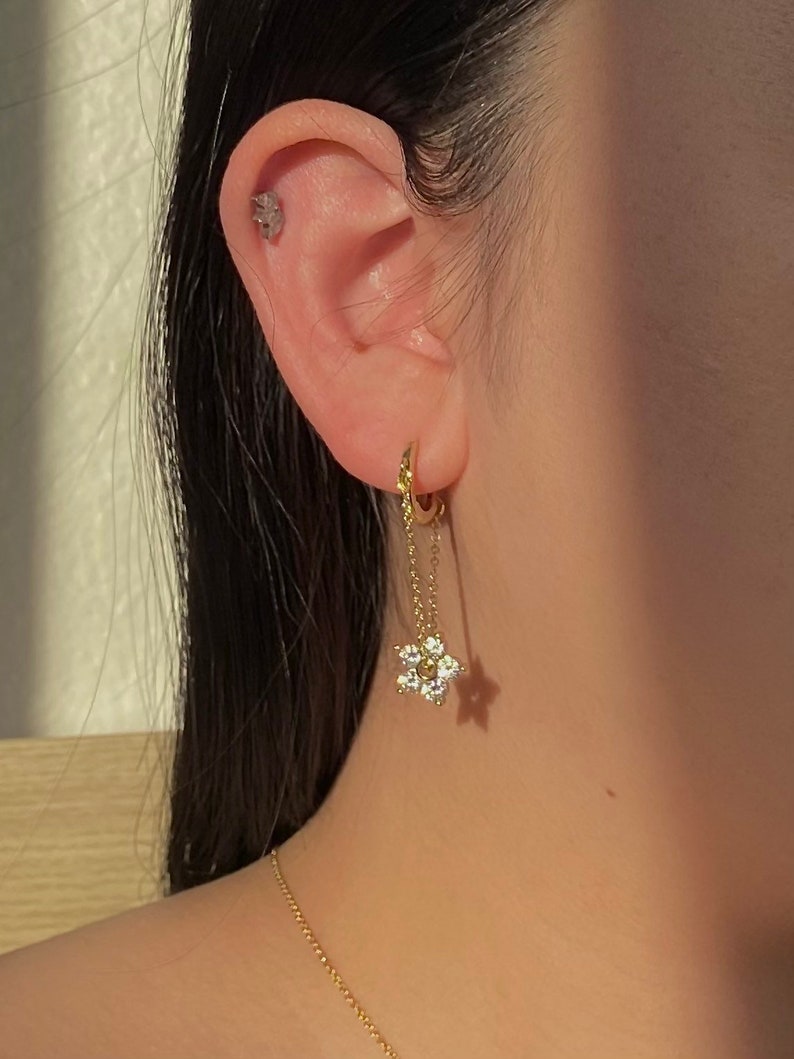 May include: Gold hoop earrings with a dangling star charm featuring clear cubic zirconia stones.