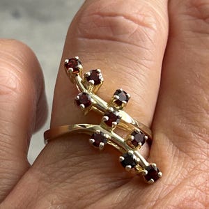 May include: A gold ring with a delicate design featuring a series of small, red gemstones set in a branch-like pattern.