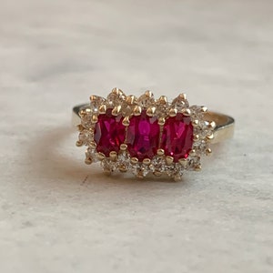 May include: A gold ring with three red ruby stones set in a cluster of small clear diamonds.