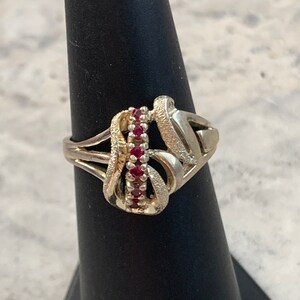 May include: A silver ring with a unique, abstract design featuring a row of red gemstones.