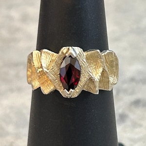 May include: A gold ring with a textured band and a red gemstone in the center.