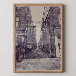 May include: A framed print depicting a narrow alleyway between brick buildings. The artwork is in a monochromatic style, with shades of gray and purple. The alleyway leads towards a distant light source, creating a sense of depth.