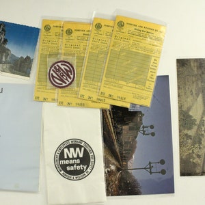 May include: A collection of vintage Norfolk and Western Railway memorabilia, including postcards, a menu, a safety sticker, and dining car checks. The postcards feature scenic views of the railway, while the menu features a Native American woman in traditional dress. The safety sticker features the text "NW means safety" and the dining car checks are yellow with black text.