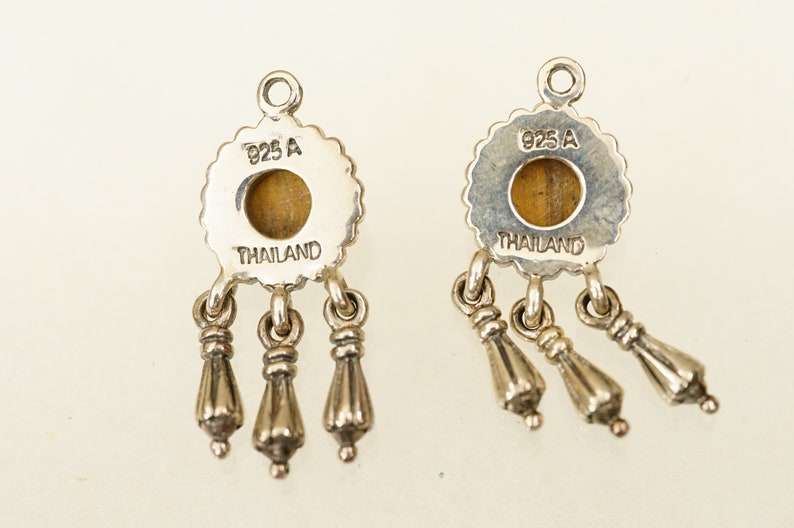 May include: A pair of silver earrings with a tiger's eye stone and three dangling charms. The back of the earrings are stamped with "925 A THAILAND".