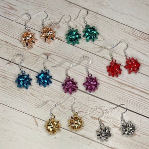 May include: Assortment of ten pairs of dangle earrings featuring a bow design. The bows are made of metallic material in various colors, including gold, silver, red, green, pink, and blue.
