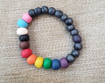 May include: A colorful beaded bracelet with a rainbow of colors, including pink, blue, black, brown, red, orange, yellow, green, blue, and purple. The bracelet also features dark gray beads.