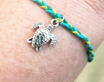 May include: A green and blue braided bracelet with a silver turtle charm.