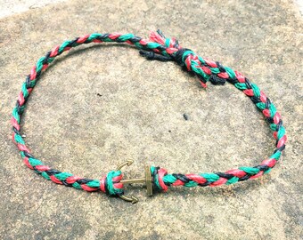 May include: A black, red, and green braided bracelet with an anchor charm.