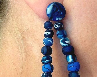 May include: Blue and white marbled polymer clay earrings with a teardrop shape. The earrings are made of multiple beads strung together.