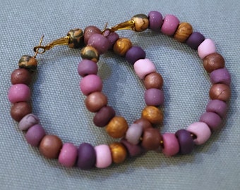 May include: A pair of hoop earrings made with purple, pink, and brown beads. The earrings are made with a variety of different sized beads.