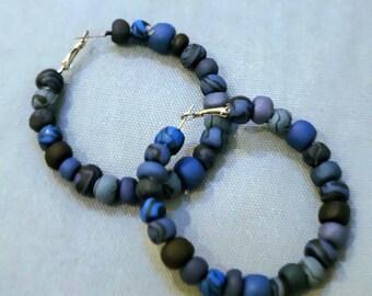 May include: A pair of hoop earrings made of blue and black patterned beads. The earrings are large and have a gold hoop.