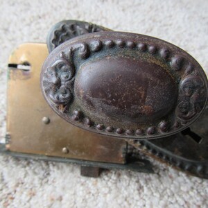 May include: A vintage door knob with a brass base and a dark brown, ornate metal handle. The handle has a decorative design with a beaded edge.