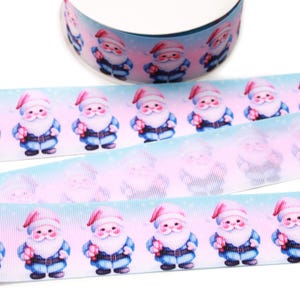 Könnte beinhalten: Eine Rolle Ripsband mit einem sich wiederholenden Muster aus Weihnachtsmannfiguren in roten Mützen und blauer Kleidung. Der Hintergrund des Bandes verläuft von Hellblau zu zartem Rosa mit einem dezenten weißen Punktmuster, das an Schneefall erinnert.