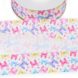 May include: A spool of white grosgrain ribbon featuring a repeating pattern of watercolour-style butterflies in shades of pink, purple, blue, and yellow, interspersed with small pink flowers and tiny blue hearts across the textured fabric surface.
