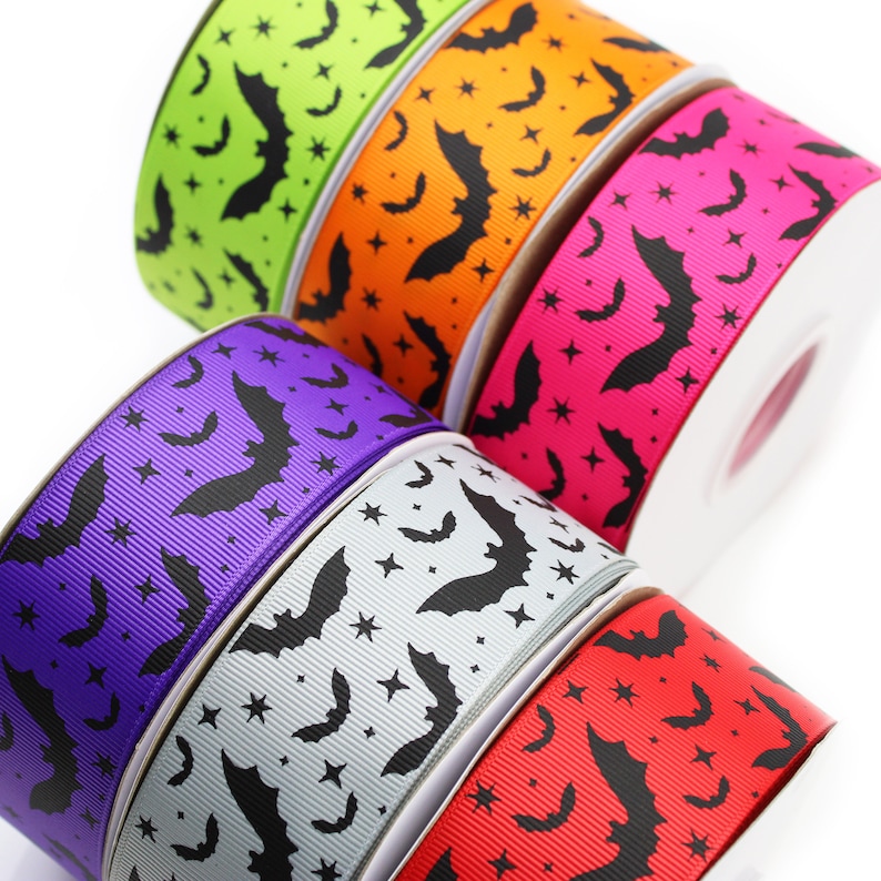 K&ouml;nnte beinhalten: F&uuml;nf Rollen Ripsband mit einem sich wiederholenden Muster aus schwarzen Flederm&auml;usen und kleinen Sternen. Die B&auml;nder sind in leuchtendem Limettengr&uuml;n, Orange, Pink, Lila, Hellgrau und Rot gehalten und jeweils fest um einen Kern gewickelt.