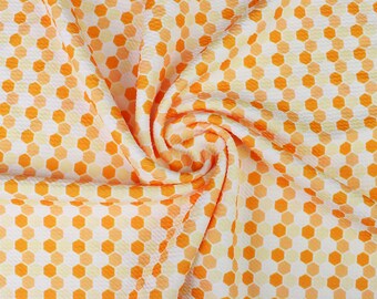 May include: A fabric featuring a repeating honeycomb pattern in shades of orange, yellow, and white. The material has a textured surface and is arranged in a spiral swirl, creating folds that highlight the geometric hexagonal design throughout.