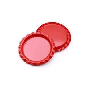 May include: Two circular metal bottle caps with a solid red finish and a serrated, crimped edge. The caps are positioned overlapping each other, showcasing the smooth, flat top surface and the distinct ridged perimeter of the bottle closure design.