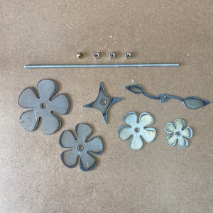 Pu&ograve; includere: Un set di materiali artigianali in metallo per realizzare un mobile. Il set comprende un'asta di metallo, quattro fiori di metallo, una stella, un pezzo di metallo curvo e quattro dadi di metallo.
