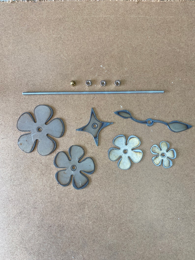 Pu&ograve; includere: Un set di materiali artigianali in metallo per realizzare un mobile. Il set comprende un'asta di metallo, quattro fiori di metallo, una stella, un pezzo di metallo curvo e quattro dadi di metallo.